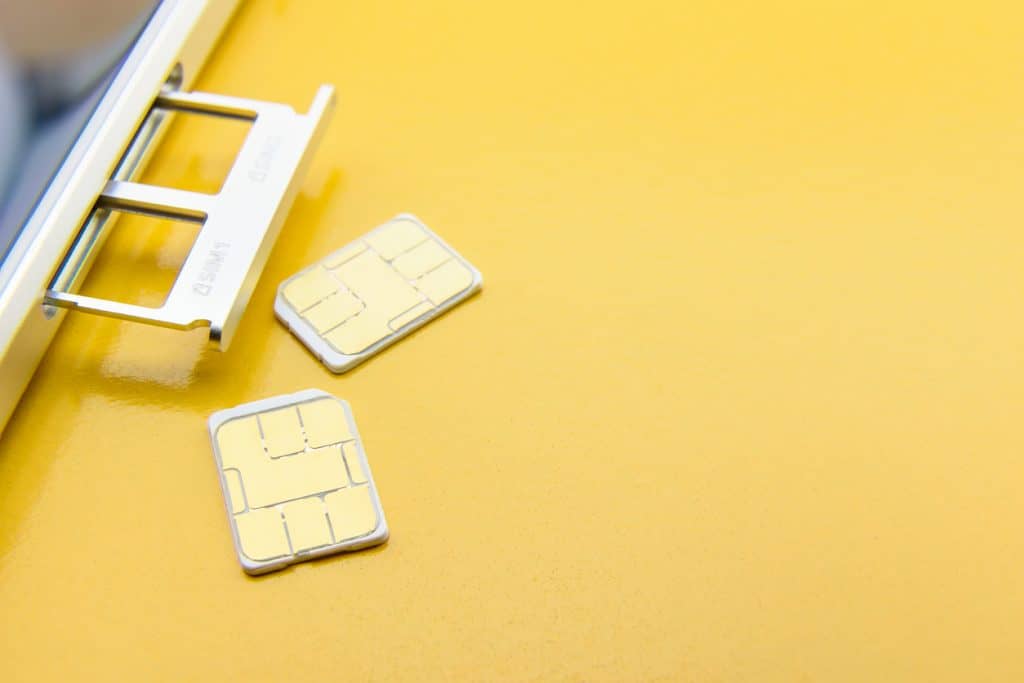Partial image of a mobile phone with the sim card slot open which reveals two slots for the sims. Also 2 sim cards displayed on a yellow background.