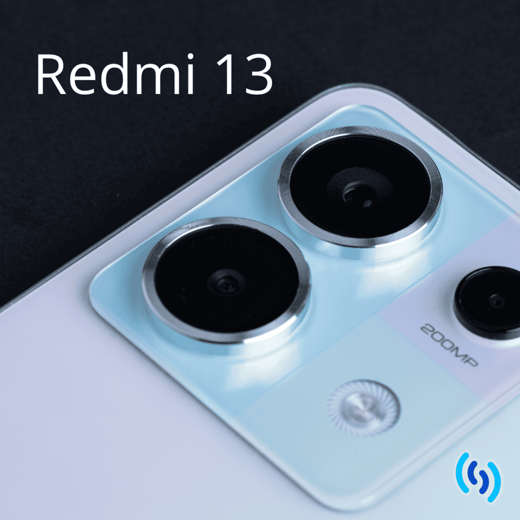 Hello this is an image of the camera portion of a Redmi Note 13 mobile phone. There are 2 circular camera lens on the phone, and a smaller lens plus a flash. The colour of the phone is a pearlescent white. The background of the image is black, and across the top in white lettering it says Redmi 13. In the bottom right hand corner is the Simpatico logo.